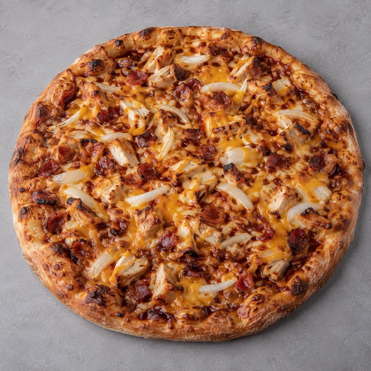 A freshly baked BBQ Chicken Pizza topped with grilled chicken, crispy bacon, melted cheddar cheese, and sliced white onions on a golden-brown crust with a smoky barbecue-style finish.